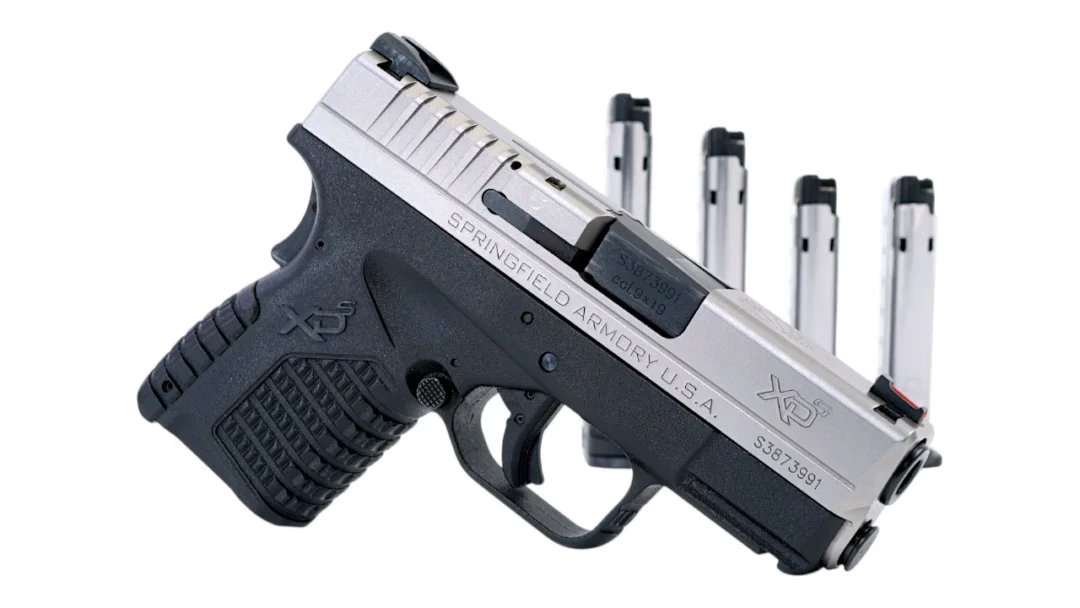Springfield Armory XD-S semi-automatic pistol with black grip and silver slide, four magazines standing upright in the background.