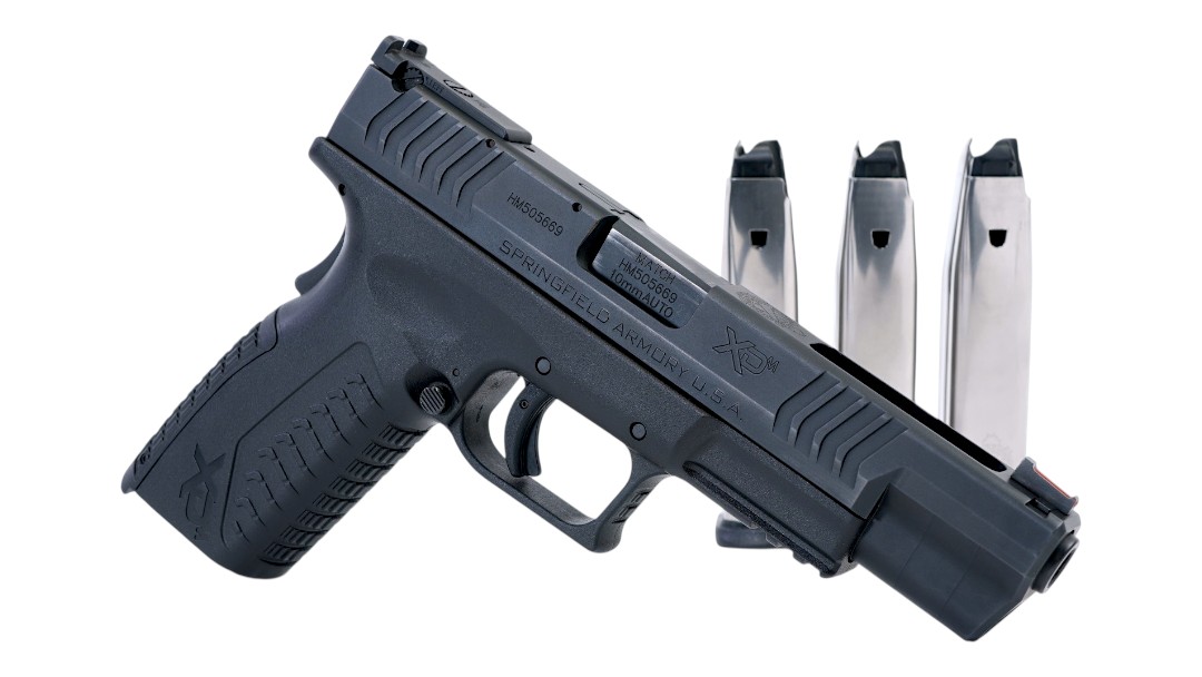 Black semi-automatic pistol with a textured grip and three magazines behind it on a white background.