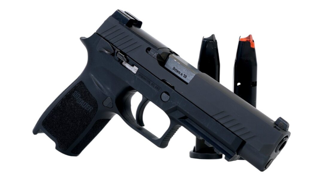 Close-up side view of a black semi-automatic pistol with two magazines in the background, 9mm x 19 markings visible on the slide.