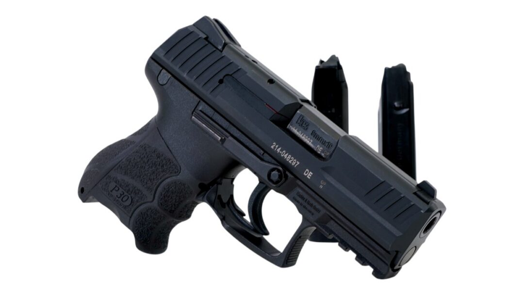 Side view of a black semi-automatic pistol with a textured grip and two magazines in the background on a white backdrop.