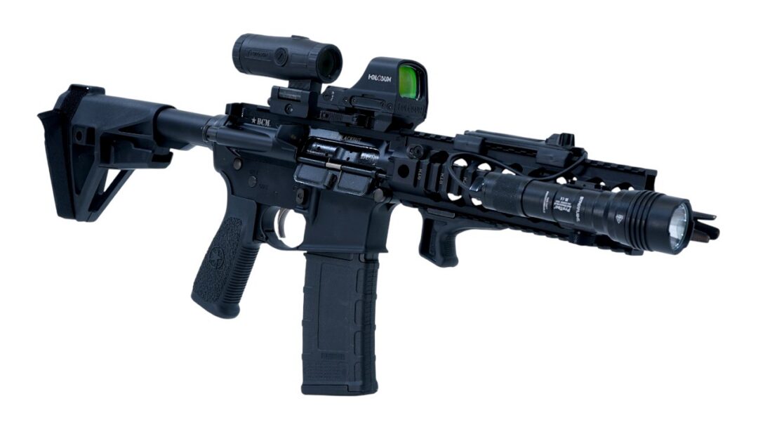 Assault-style rifle with a mounted scope, foregrip, and front flashlight, shown in side view on a white background (informational image).