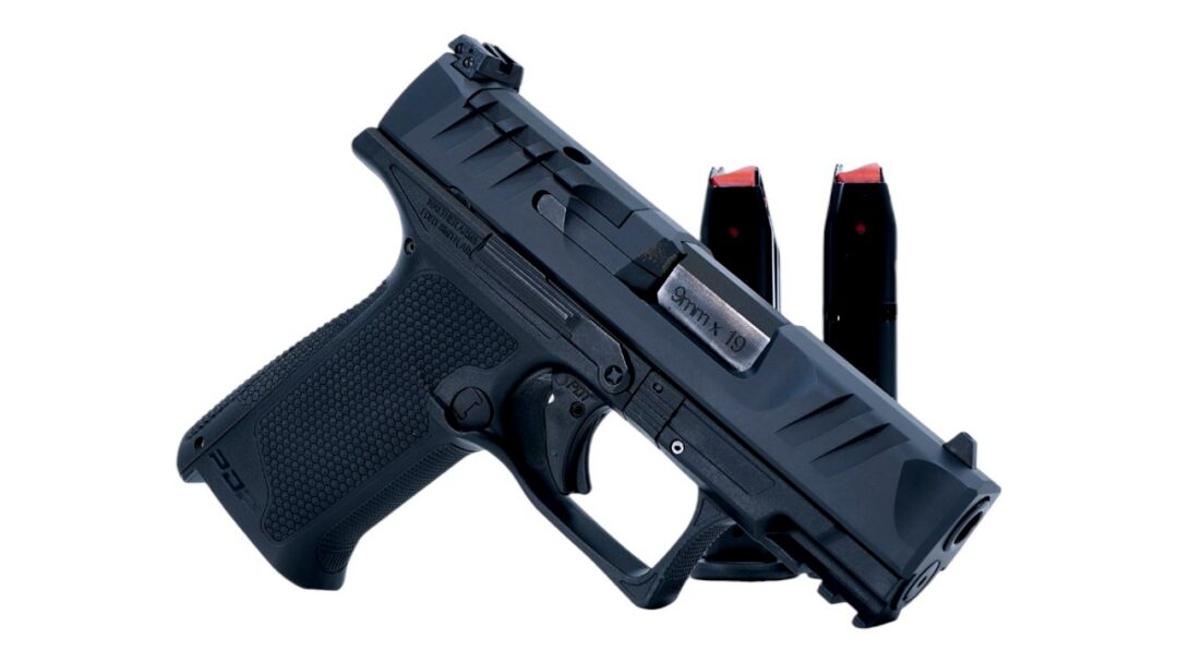 Black semi-automatic pistol with two magazines behind it on a white background, side view.