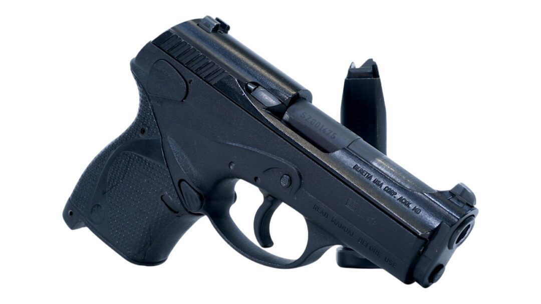 Side view of a black compact semi-automatic pistol with a detached magazine beside it on a white background, showing the grip and trigger.