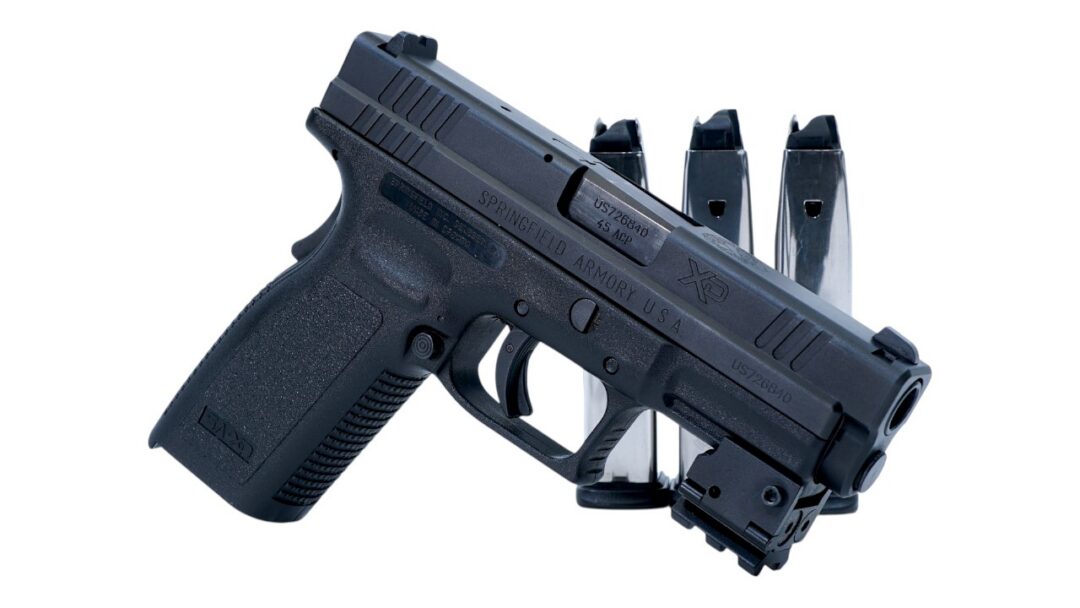 Black semi-automatic pistol with three magazines standing behind it on a white background (Springfield Armory, .45 ACP).